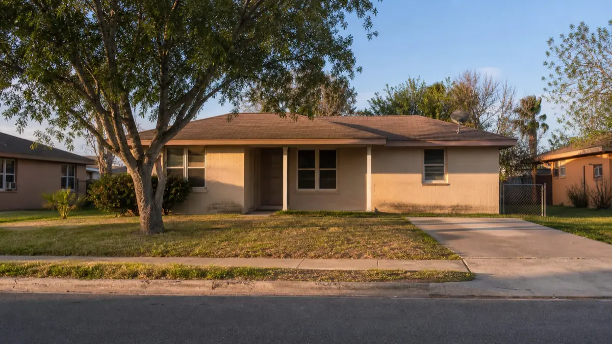 A modest single-story rental house on a quiet South Texas street in worn but decent condition, lit by late afternoon light